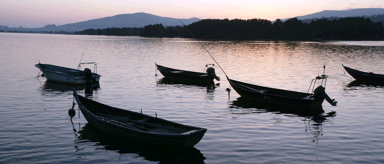 Fotografia de um entardecer no estuário do rio Minho, em Caminha, com alguns barcos de pesca no leito do rio