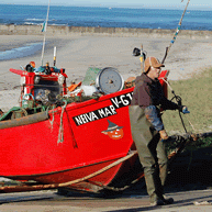 Pescador de pé junto ao seu barco numa praia